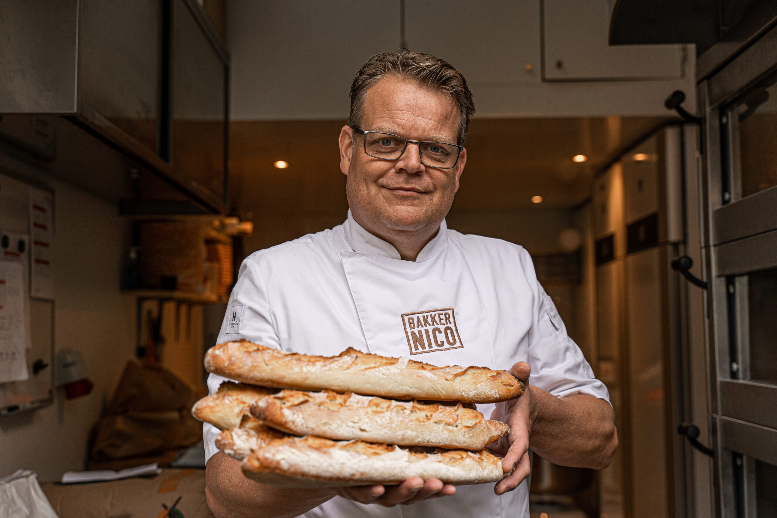 Bakker Nico met vers gebakken broden in de bakkerij